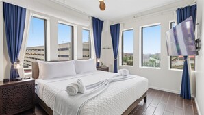 Habitación de hotel con una cama grande, un televisor y vistas a edificios a través de las ventanas.