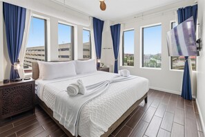 Habitación de hotel con una cama grande, un televisor y vistas a edificios a través de las ventanas.
