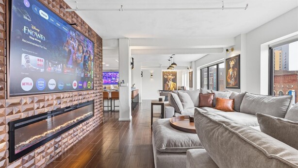Una sala de estar moderna con un televisor de pantalla plana grande montado en una pared de ladrillo, un sofá modular gris y piso de madera.