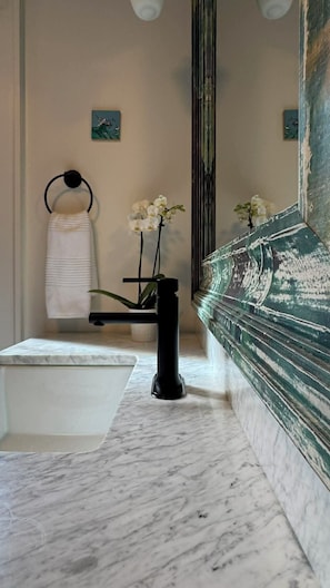 A bathroom with a marble sink, a black towel ring, a white towel, and a vase with white flowers.