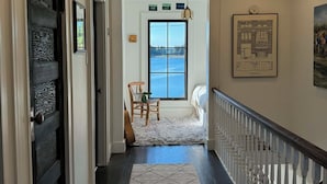 A hallway with a patterned rug, a view of the sea through a window, and a framed architectural drawing on the wall.