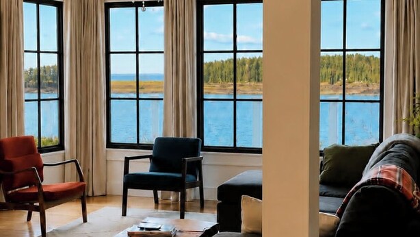 A spacious living room with a large window offering a view of a lake and forest, a chandelier, and modern furniture.