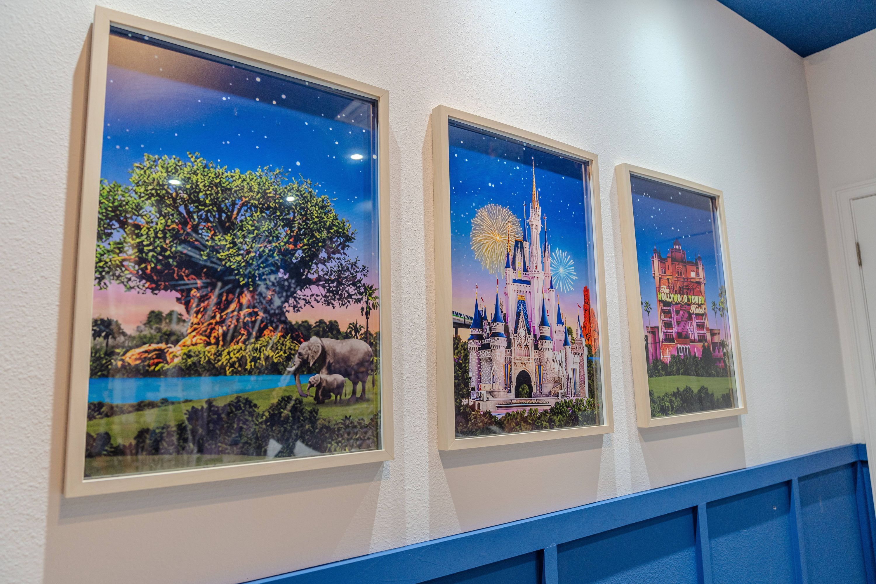 Tres cuadros en una pared, cada uno mostrando una escena distinta: un árbol con elefantes, un castillo con fuegos artificiales y un edificio con un cartel.