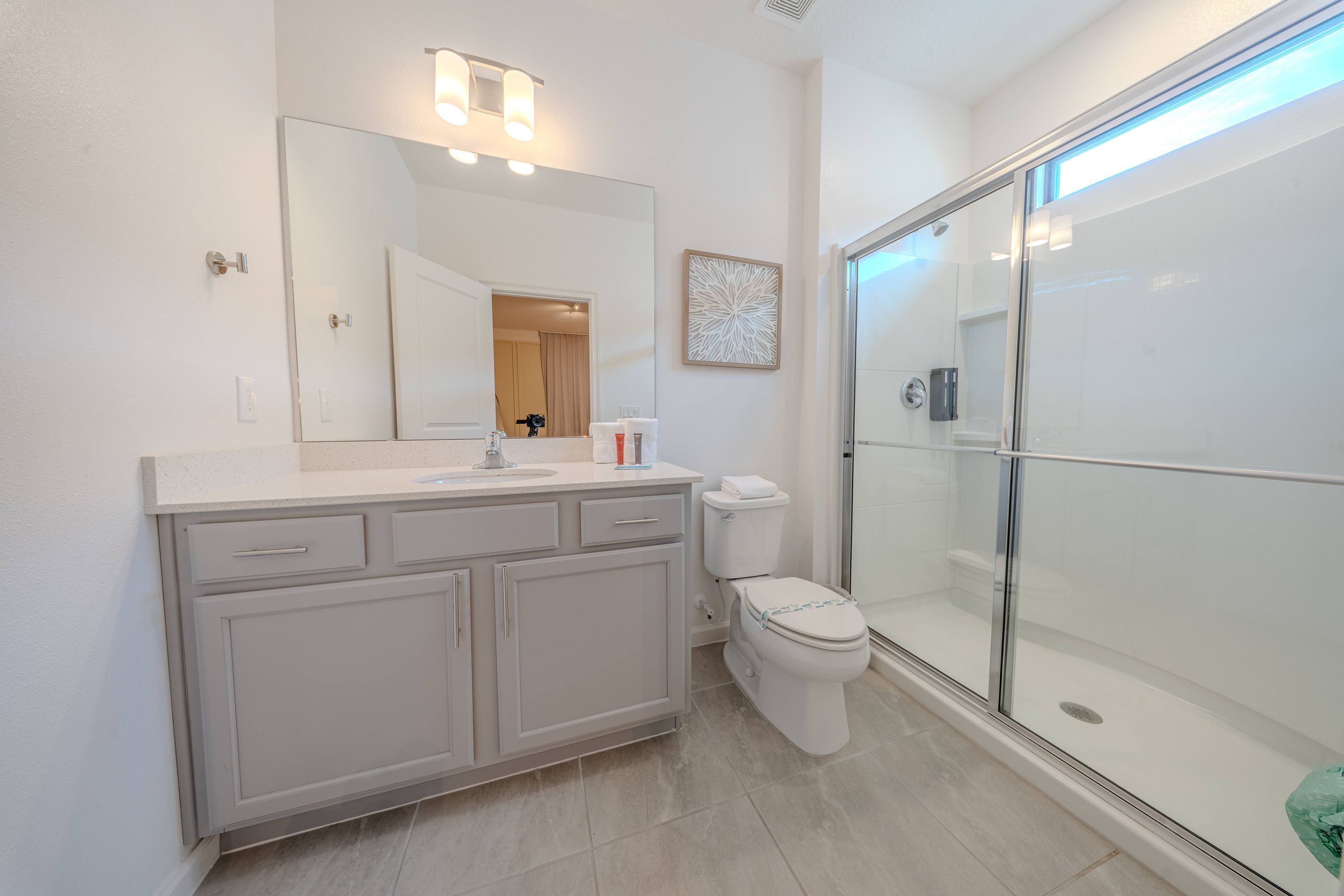 Une salle de bain moderne avec un grand miroir, des toilettes, un espace douche et un meuble-lavabo avec des tiroirs.