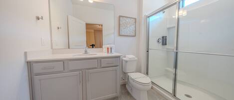 Une salle de bain moderne avec un grand miroir, des toilettes, un espace douche et un meuble-lavabo avec des tiroirs.