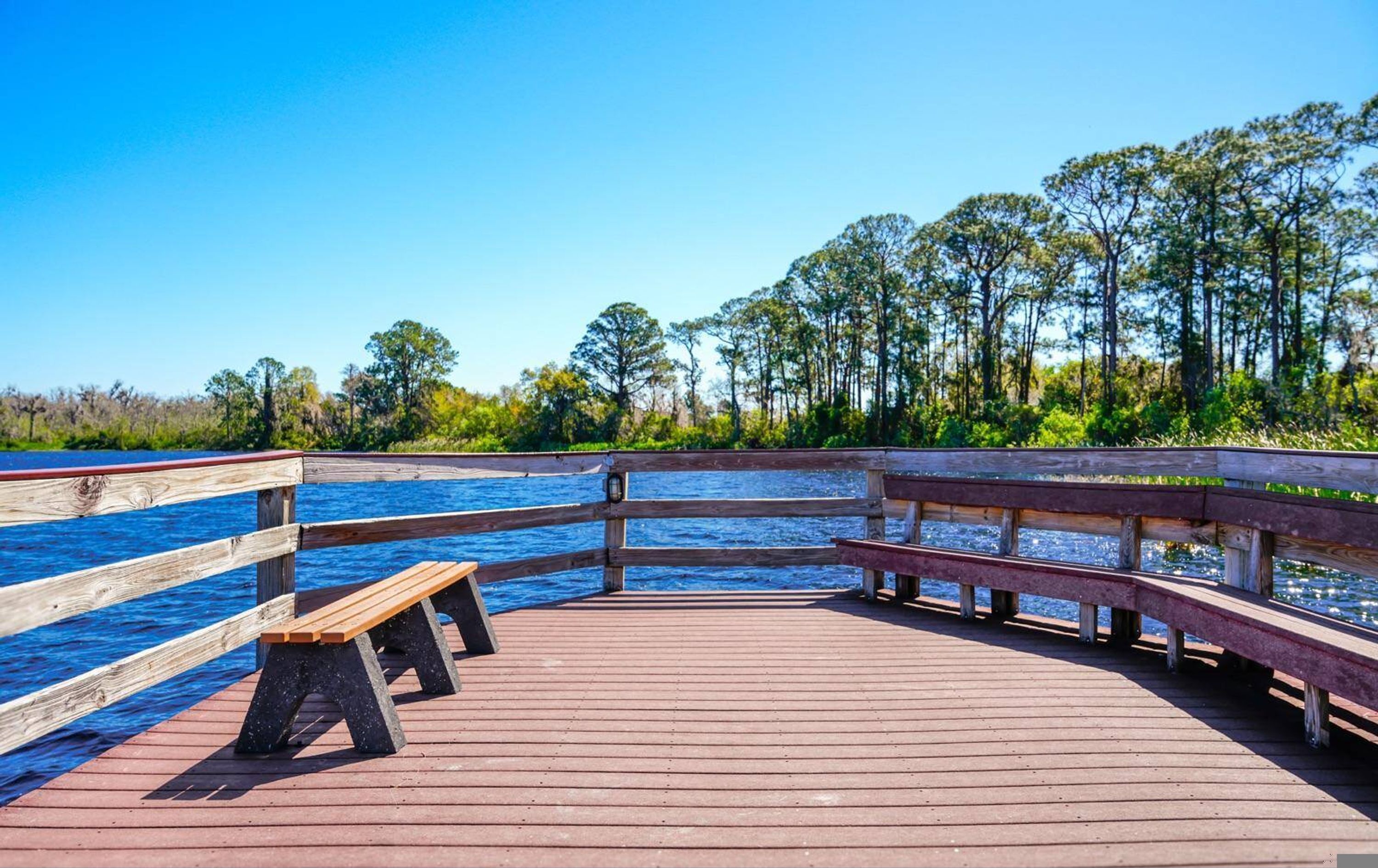 A wooden pier with benches, extending over a body of water, surrounded by trees.