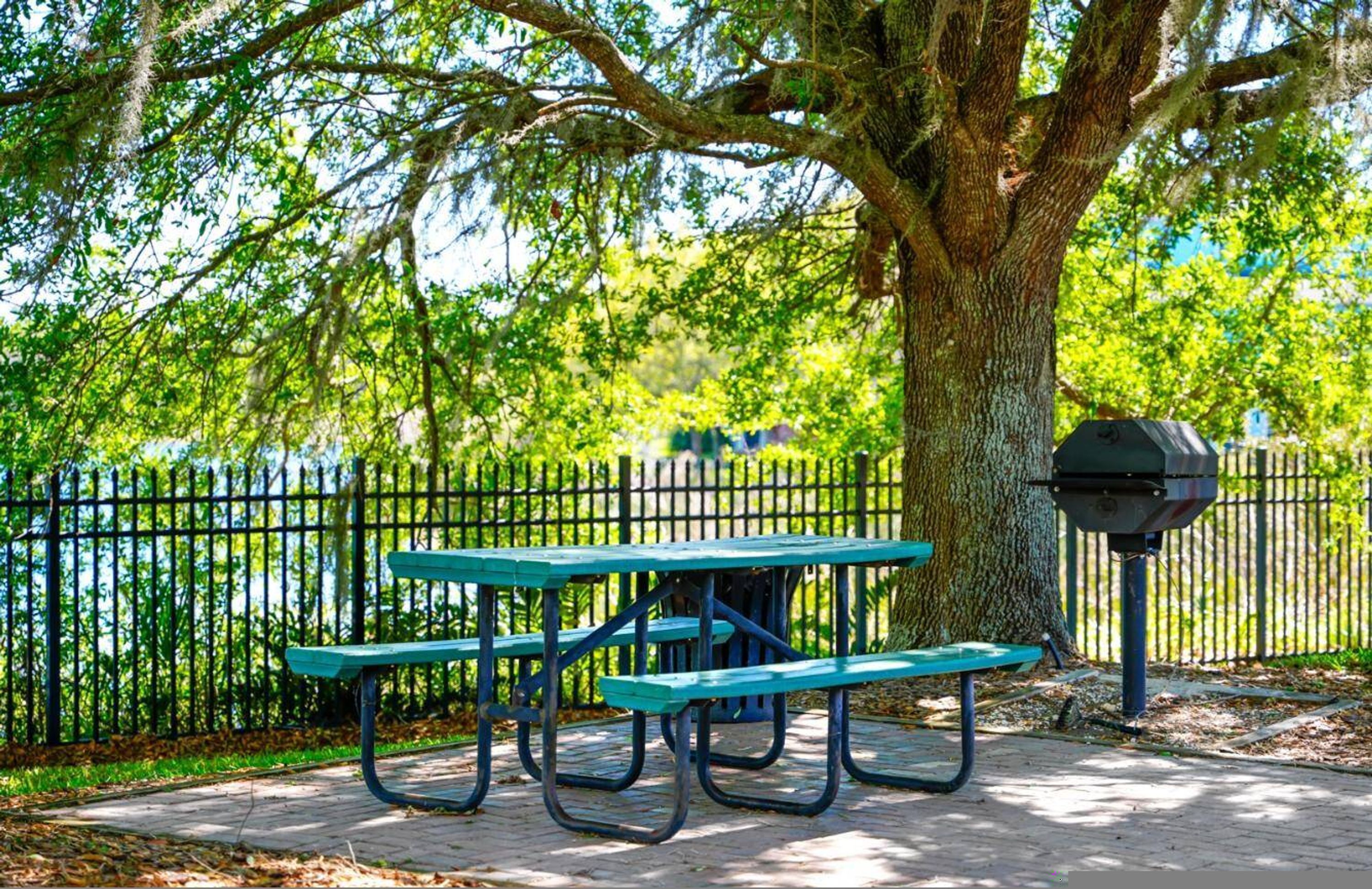 Eine Parkbank mit Grill, Baum und Zaun.