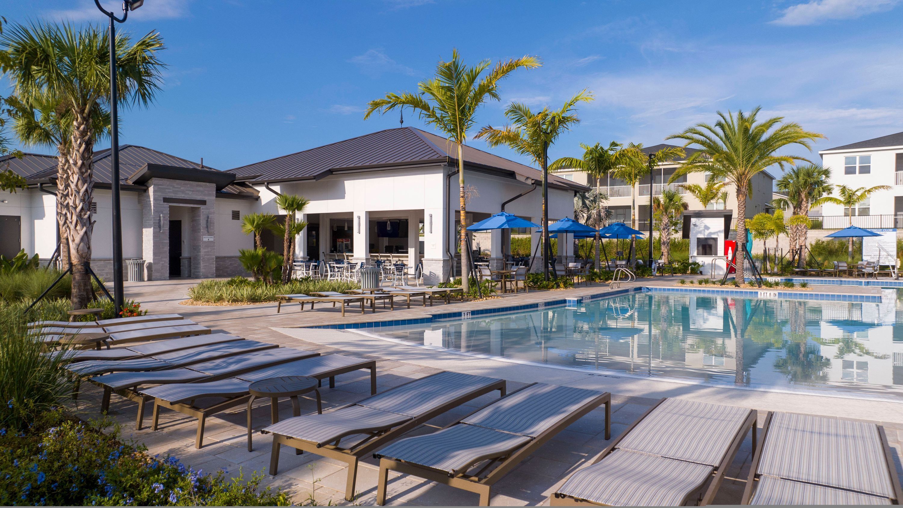 A pool area with lounge chairs, umbrellas, and a building with a covered patio.