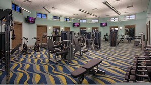 Un gimnasio con equipo de ejercicio, alfombra estampada y varias pantallas de televisión en las paredes.