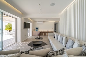A modern living room with a sofa, a coffee table, and a kitchen area in the background. - Villa Med in Mykonos (Mykonos)