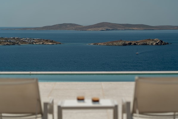 A poolside view with lounge chairs, a clear blue sea, and distant landforms. - Villa Med in Mykonos (Mykonos)