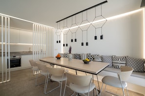 A modern kitchen with a built-in oven, a dining area with a long table and chairs, and a wall-mounted light fixture. - Villa Med in Mykonos (Mykonos)