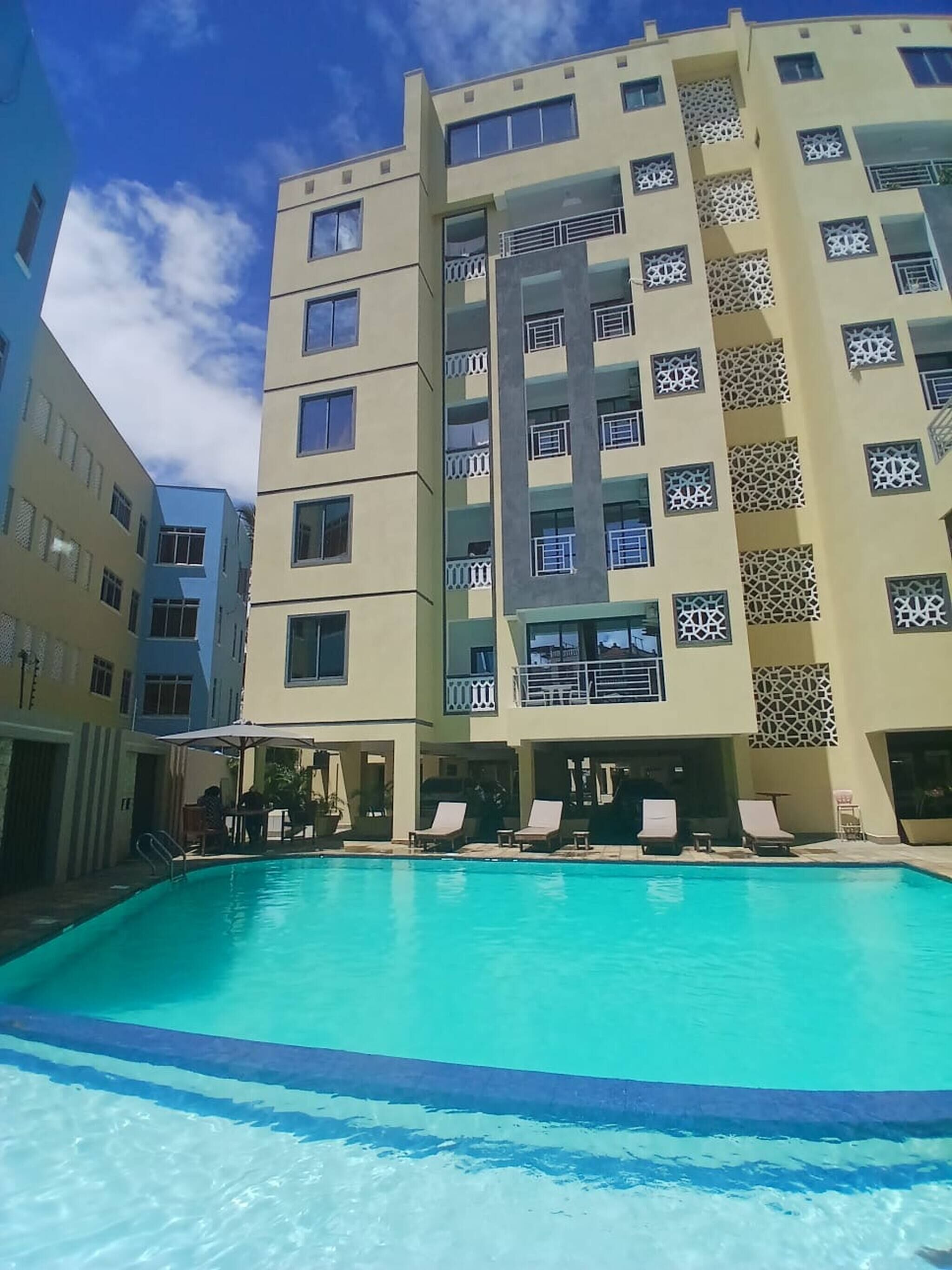 A multi-story hotel with a swimming pool, balconies, and a clear sky.