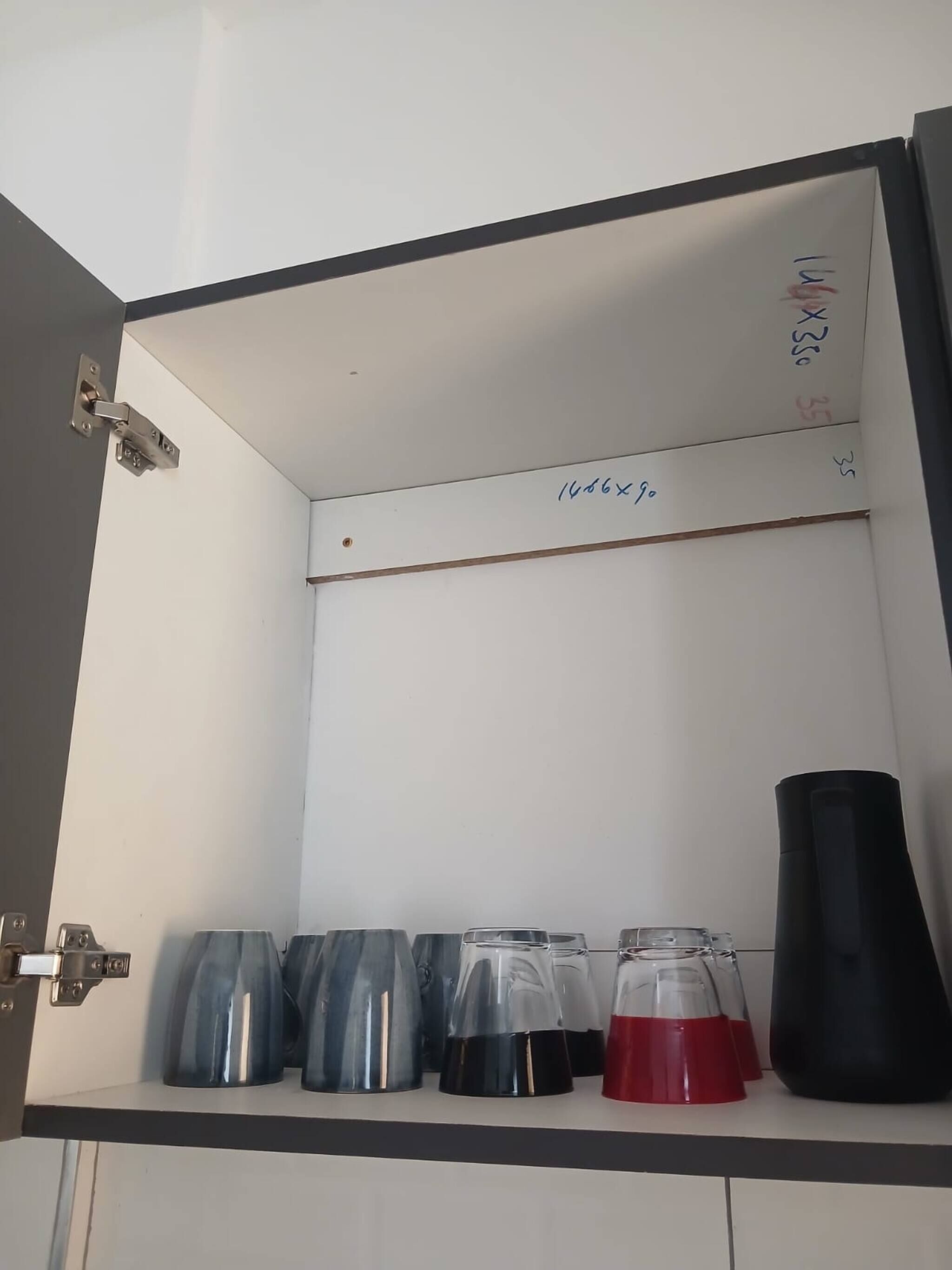 Un meuble avec une porte à charnières, une étagère contenant divers récipients et un texte manuscrit sur la porte.
