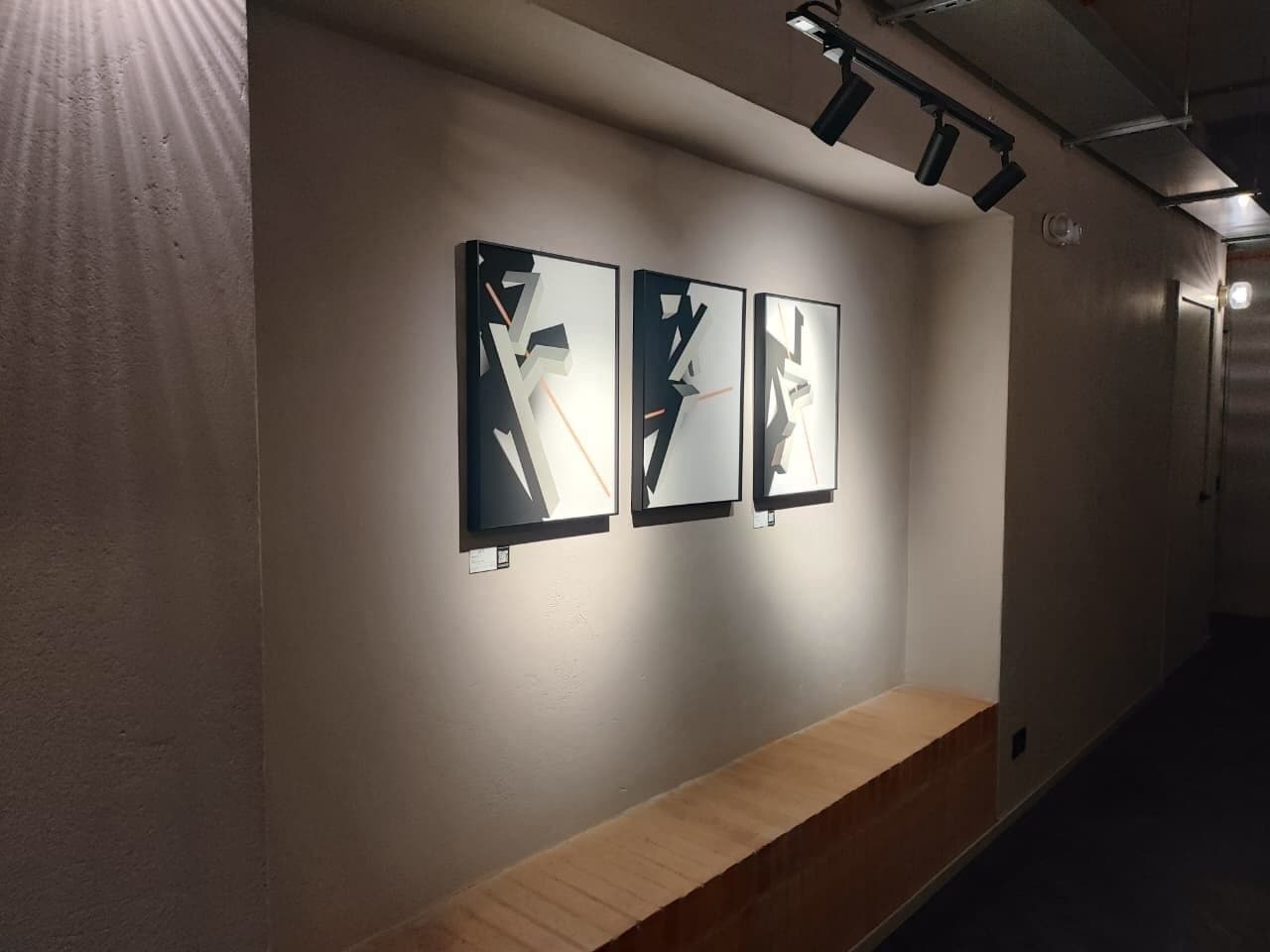 Ein Flur mit drei gerahmten Kunstwerken an der Wand und einer hölzernen Bank.