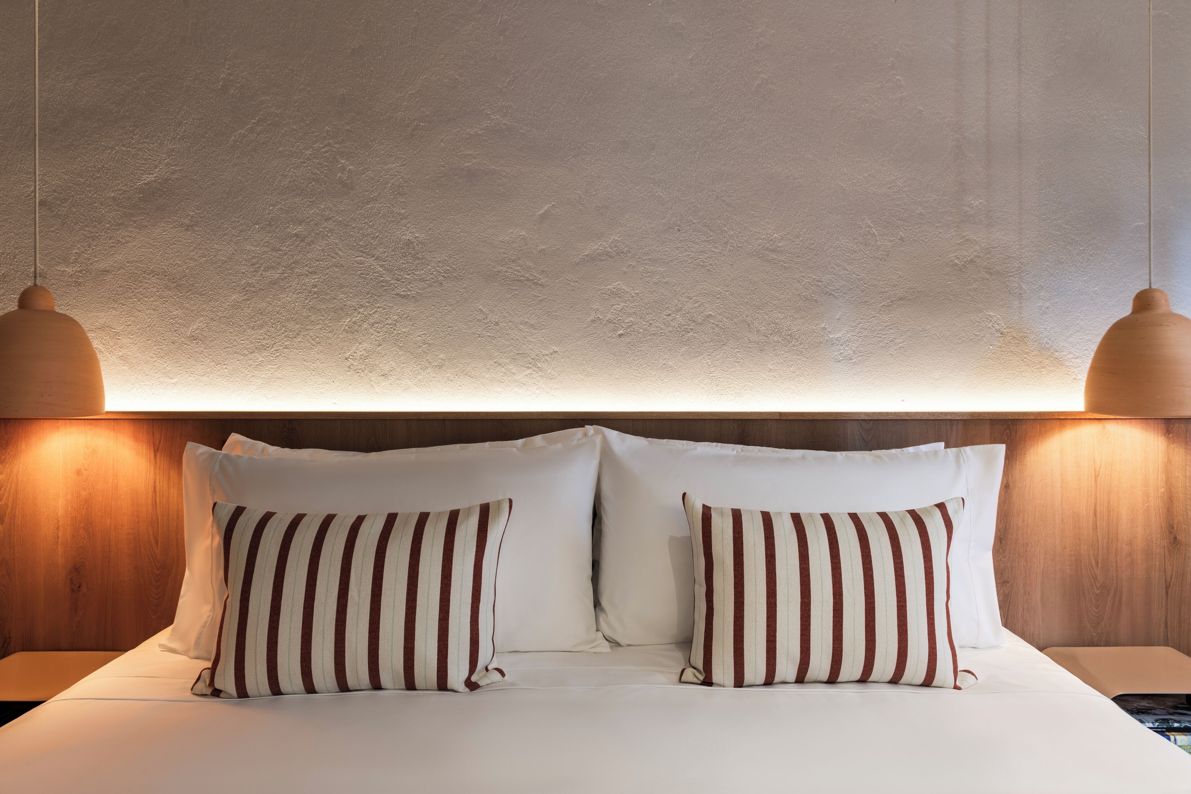A neatly made bed with two pillows, a wooden headboard, and two wall-mounted lamps.
