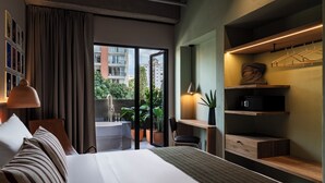 Habitación de hotel con cama, escritorio, silla, perchero y vistas al exterior.