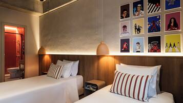 A hotel room with two beds, a nightstand, a wall with framed pictures, and a wooden headboard.