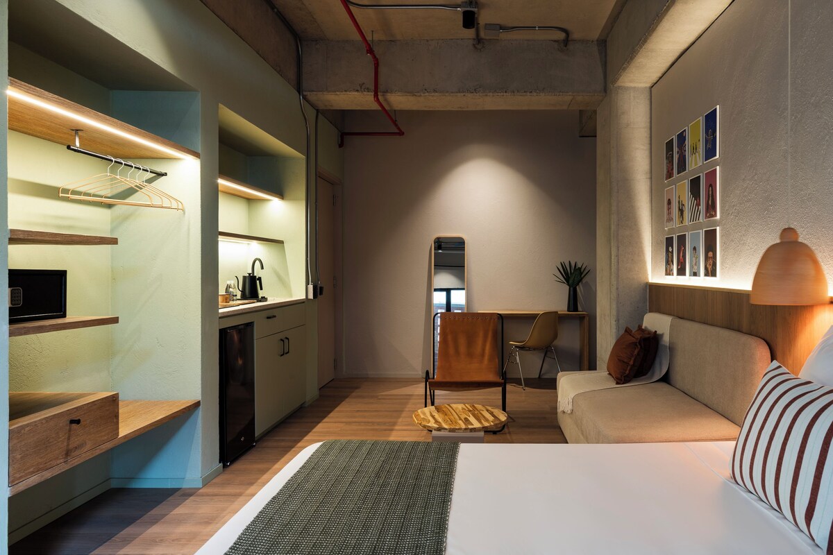 A modern hotel room with a kitchenette, a sofa, a dining table, and a large mirror.