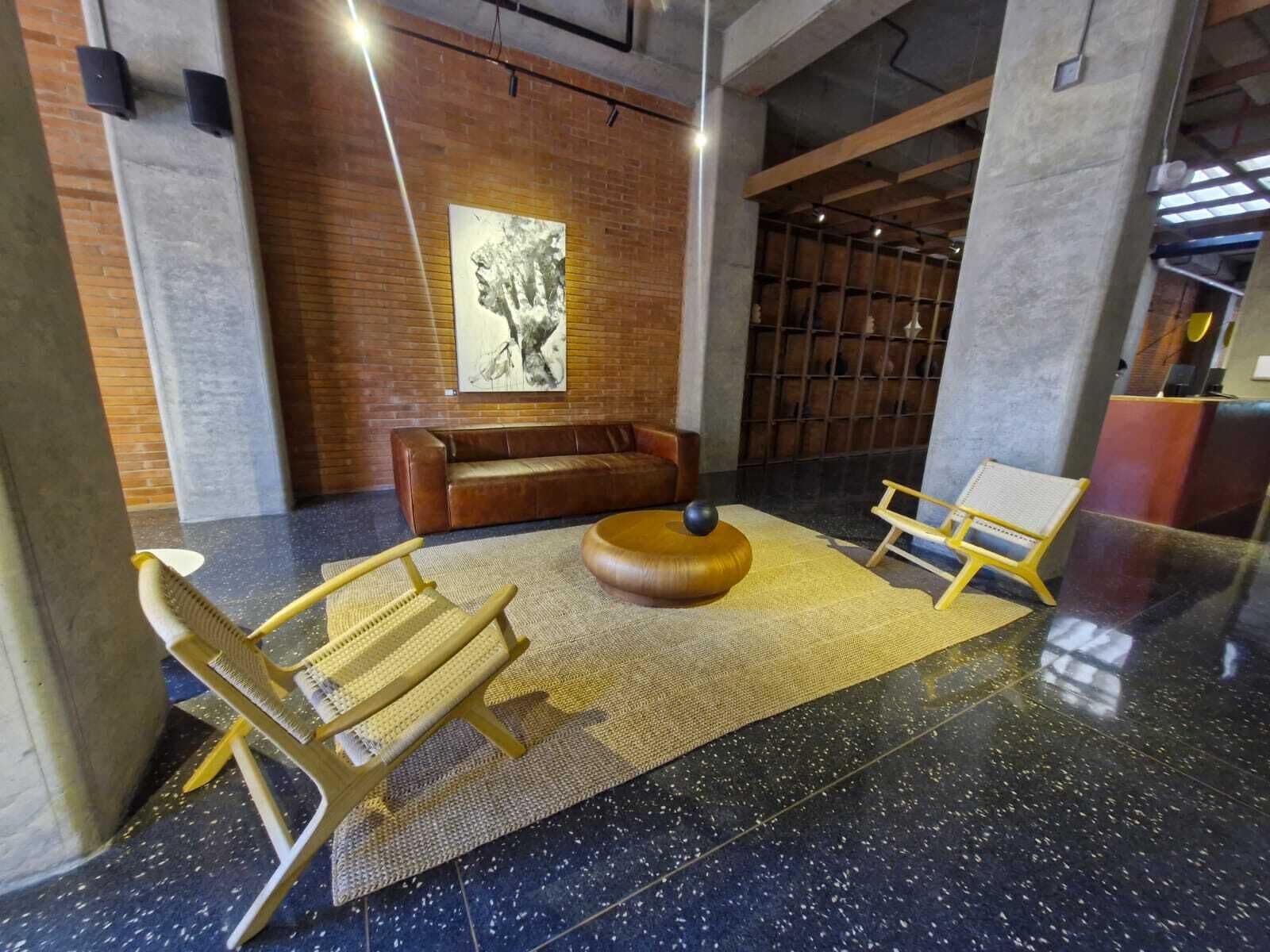 A modern lobby with a leather sofa, a wooden chair, a round table, and a large abstract painting on the wall.