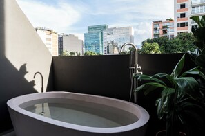 A modern bathroom with a freestanding bathtub, a shower, and a view of the cityscape. - Obra Hotel (Medellin)
