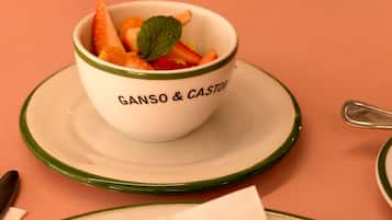 A bowl of fruit on a plate with a green rim, placed on a pink table.