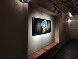 A hallway with a wall-mounted artwork, a bench, and a ceiling light fixture.