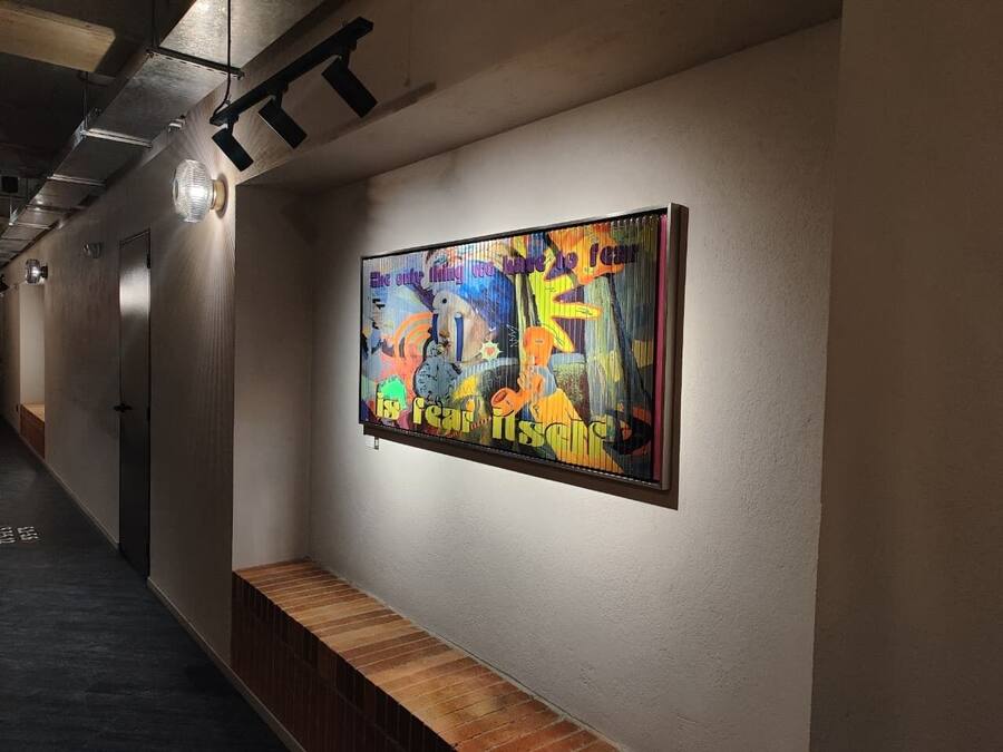 Un pasillo con un cuadro abstracto y llamativo en la pared y un banco de madera.