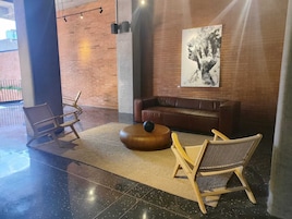 A lobby area with a brown leather sofa, two wicker chairs, a round wooden table, and a black sculpture.