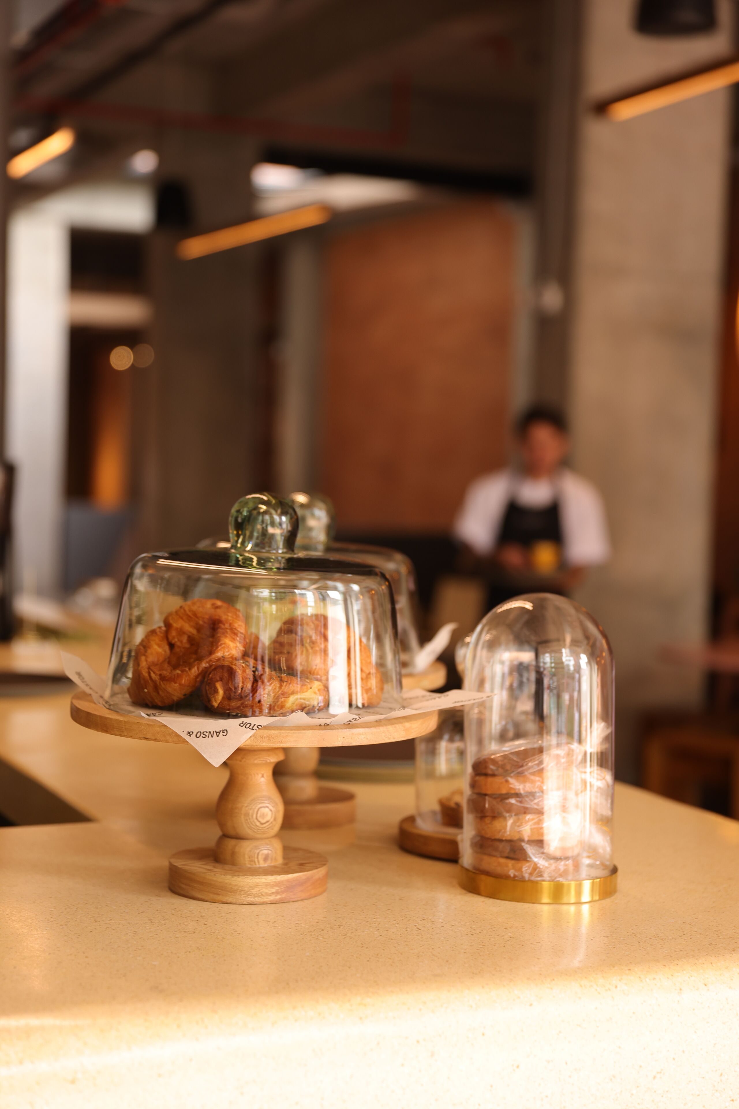 Une vitrine de pâtisserie présentant des viennoiseries sous des cloches de verre, le tout posé sur un présentoir en bois.