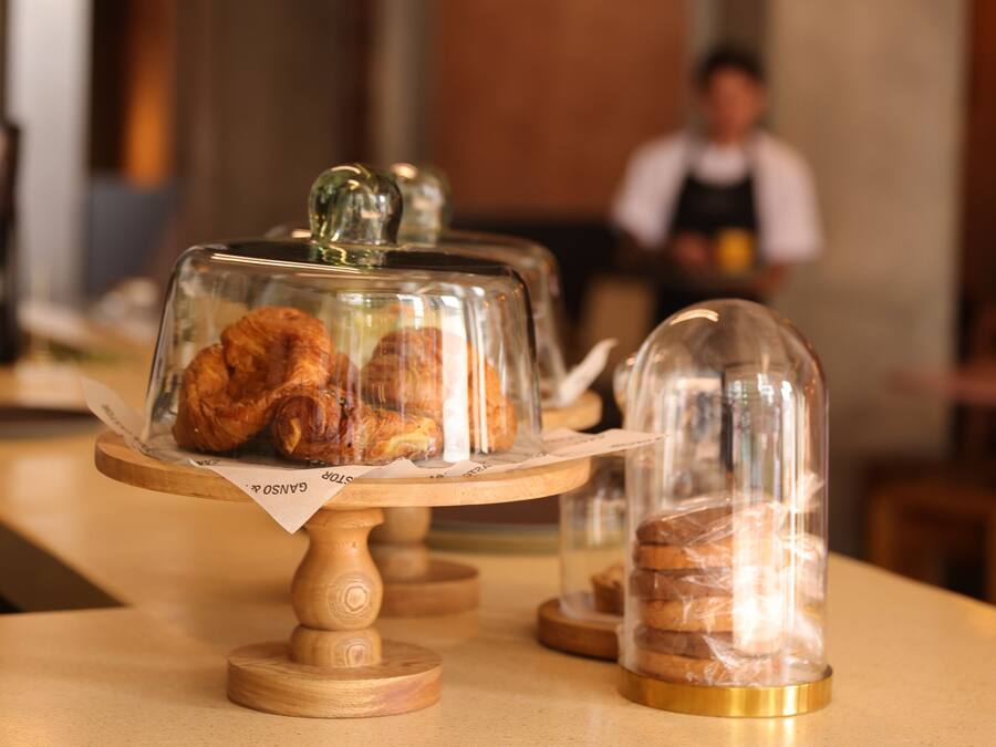 Une vitrine de pâtisserie présentant des viennoiseries sous des cloches de verre, le tout posé sur un présentoir en bois.