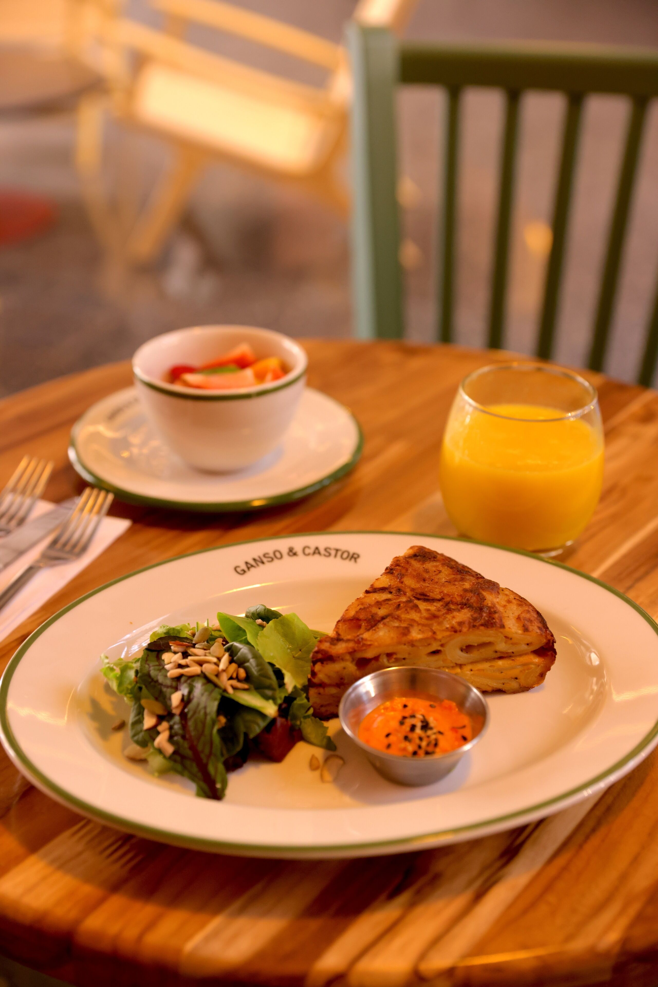 A meal consisting of a grilled sandwich, a salad, a bowl of soup, and a glass of orange juice on a wooden table.