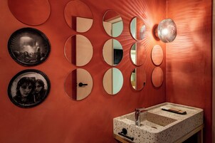 Un baño con pared roja, varios espejos redondos, un lavabo con encimera moteada y un perchero para toallas.