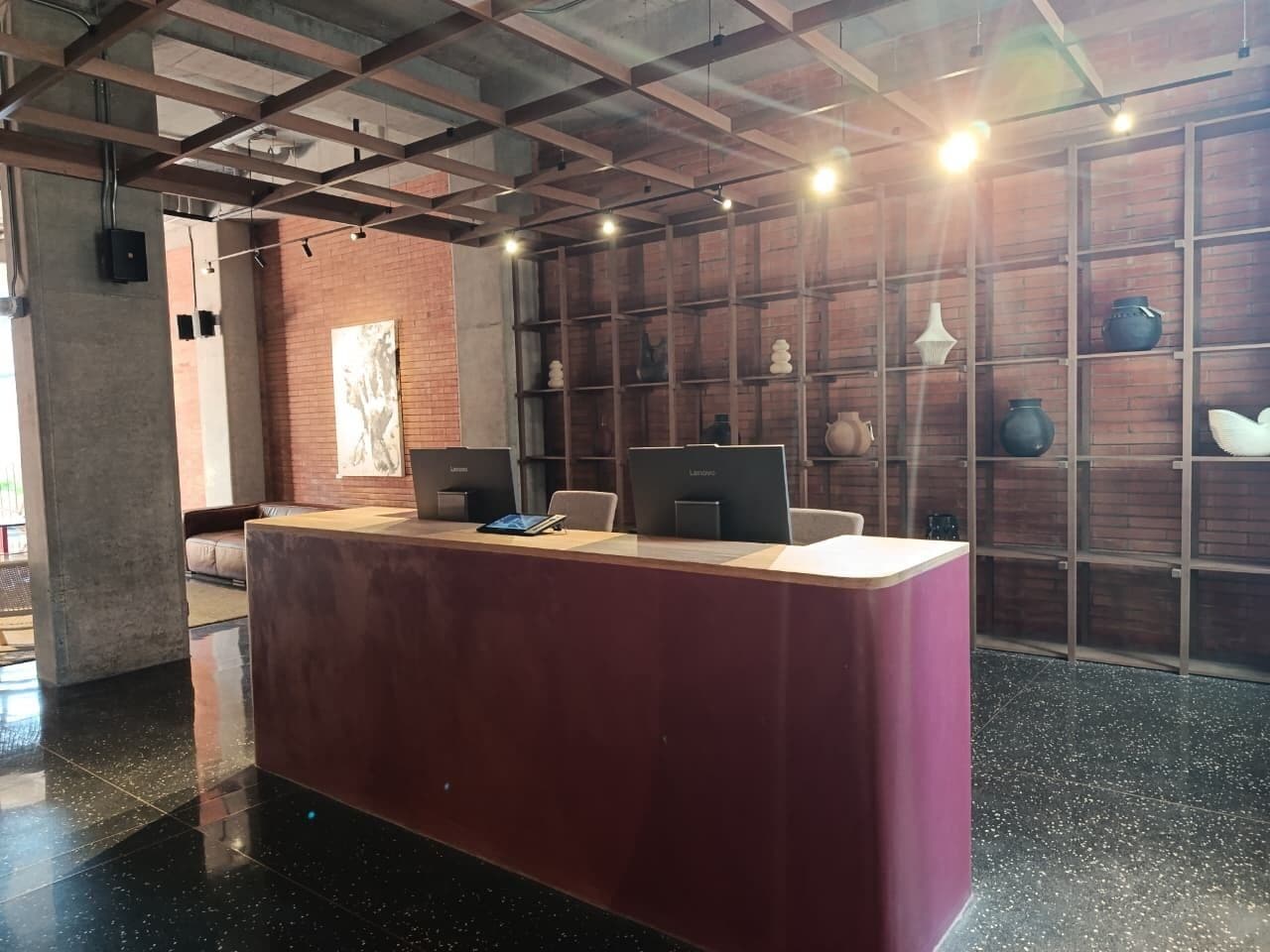 Un comptoir d’accueil avec des ordinateurs, un espace détente avec des sièges et un mur en briques doté d’étagères.
