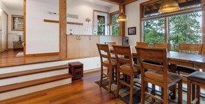 A wooden dining area with a table and chairs, a staircase, and a view of greenery outside.