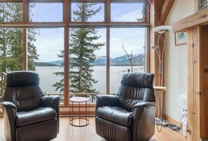 A room with two leather recliners, a small round table, and a view of a lake and mountains through large windows.