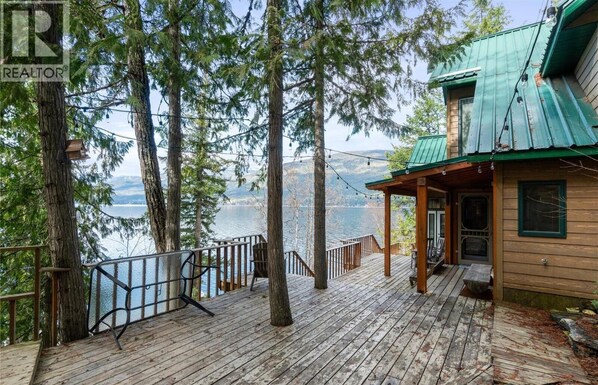 A wooden deck with a railing overlooking a lake, surrounded by tall trees.