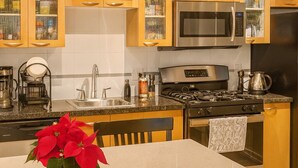 A kitchen with wooden cabinets, a stainless steel stove, and a dining area with a table and chairs. - Middle of DOWNTOWN VANCOUVER INDEPENDENT APARTMENT SLEEPS 4 (Vancouver)