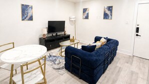 Uma sala de estar moderna com uma mesa redonda de mármore, um sofá azul e uma televisão de tela plana.