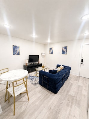 Una sala de estar moderna con una mesa redonda de mármol, un sofá azul y un televisor de pantalla plana.