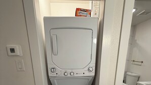 Uma lavanderia compacta e branca com máquina de lavar e secadora frontais, painel de controle com várias configurações e o nome da marca visível na parte superior da secadora.
