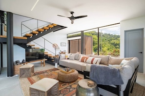 Ein modernes Wohnzimmer mit Treppe, Sofa, Couchtisch und Blick auf Grünflächen.