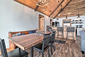 A dining area with a wooden table and chairs, a kitchen in the background, and a high ceiling with exposed beams. - Red Door House, Rabun Gap (Rabun Gap)