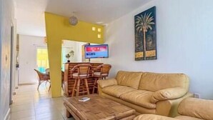 Ett vardagsrum med en soffa, ett soffbord, en takfläkt och en tv som hänger på väggen.