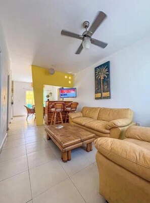 Ein Wohnzimmer mit einer Couch, einem Couchtisch, einem Deckenventilator und einem Fernseher an der Wand.