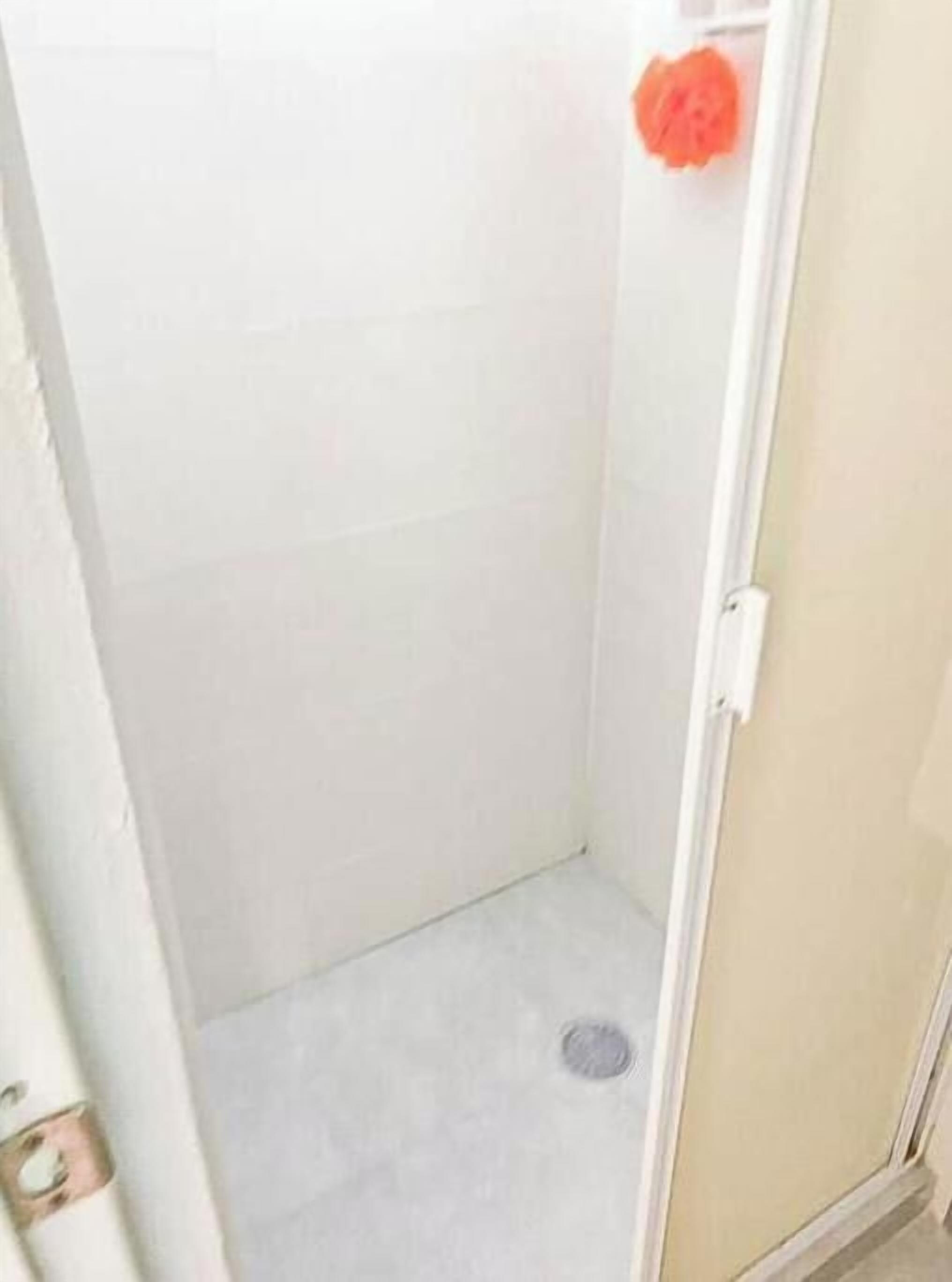 A small, enclosed bathroom with a white tiled wall, a metal door, and a visible drain.