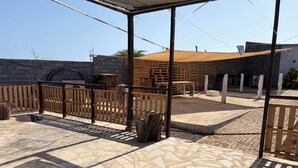 An outdoor patio area with a wooden fence, a covered seating area, and a patterned stone floor.