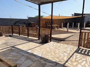 Un patio al aire libre con cerramiento de madera, zona cubierta con asientos y suelo de piedra con diseño.