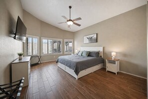 Ein Schlafzimmer mit einem Bett, einem Schreibtisch, einem Sessel, einem Deckenventilator und einem an der Wand befestigten Fernseher.