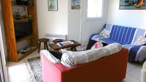 Een woonkamer met een rode bank, een blauw gestreepte zitting, een houten boekenkast, een klein tafeltje en een vloerlamp.